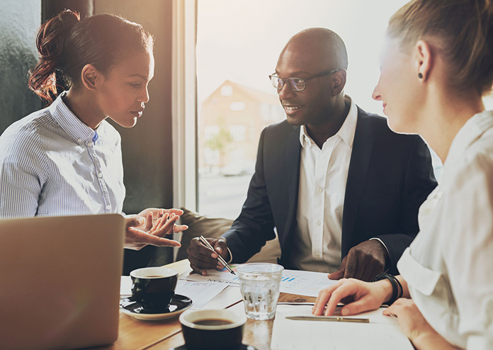 Meeting, three people sit at a table with coffee, laptops, and paperwork. Best Small Business Bank